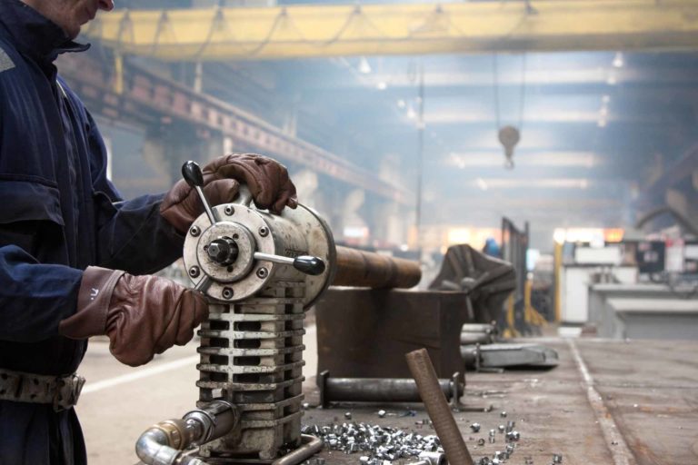 A man wearing thick leather gloves and using machinery A man wearing thick leather gloves and using machinery